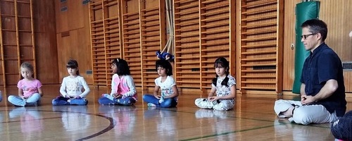 Kinder sitzen in der Meditationsübung, gemeinsam mit dem Falun Dafa-Praktizierenden