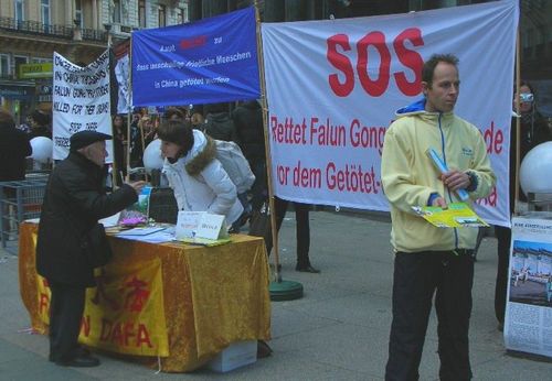 Aufbau des Infostandes auf dem Stephansplatz in Wien. Viele Banner informieren über die Dringlichkeit der Beendigung der Verfolgung. Links hinten ist zu sehen wie mit einem Käfig Foltermethoden demonstriert werden, welche Falun Gong Praktizierende in China ausgesetzt sind.