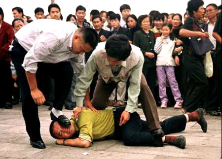 Ein Bild mit starker Aussagekraft. Ein sich nicht wehrender Falun Gong Praktizierender wird von Polizisten am Platz des Himmlischen Friedens in Peking brutal festgenommen. Er wollte friedlich für ein Ende der Verfolgung asppellieren. Ringsum Menschen, die, getäuscht von der KP­Propaganda, die wahre Tragweite dieser Unterdrückung nicht klar erkennen kann.